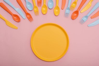 Renkli plastik sofra : çatal, bıçak, kaşık ve pembe arka plan üzerinde sarı plaka