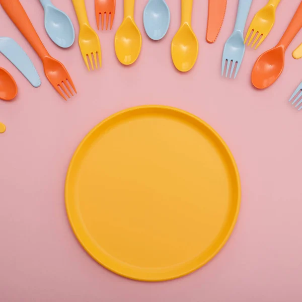 Vaisselle colorée : cuillère, couteau, fourchette et assiette jaune sur fond rose . — Photo