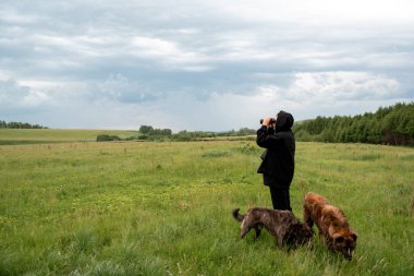 Uzağa bakan dürbünlü bir adam. Tarlada iki köpek varken. Yaz.