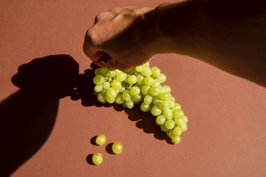 Eli üzüm tutuyor. Kahverengi masa. Doğal güneş ışığı.