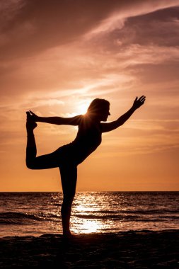 Gün batımında Maui sahilinde yoga yapan bir kadın.