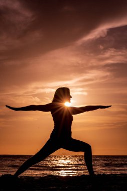 Gün batımında Maui sahilinde yoga yapan bir kadın.