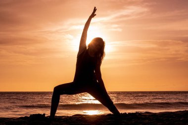 Gün batımında Maui sahilinde yoga yapan bir kadın.