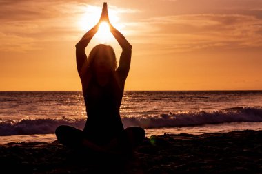 Gün batımında Maui sahilinde yoga yapan bir kadın.