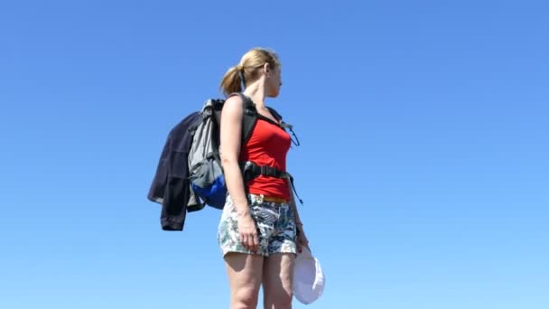 細身の女の子旅行者のバックパックを青い空を背景に立って 辺りを見回す — ストック動画