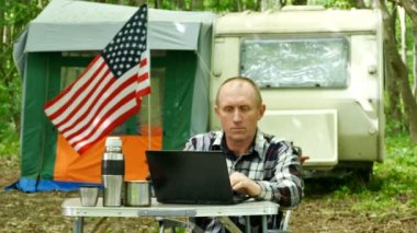 4 k. Amerikalı bir adam gezgin çalışır laptop karavan kamp yakınındaki ve gülümse. Serbest hayat