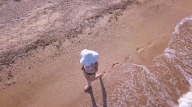 4k hava. Kız, kadın mayo ve beyaz şapka etrafında sinek. Yürüme, sahil, üstten görünüm