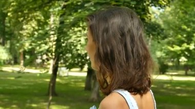           Rretty kadın yürüyüş Şehir Parkı, dalga saç ve gülümsüyor. Ağır çekim, sürekli çekim