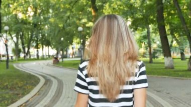           4k. İnce kadın stand ve yaz şehir parkı gülümseme. Sürekli çekim, arkadan görünüm