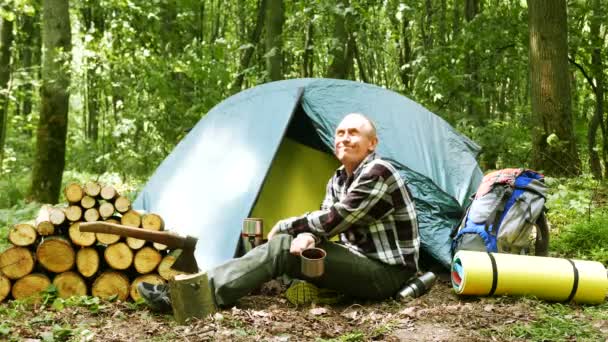 微笑成年男子游客在帐篷附近休息在木和喝茶或咖啡 — 图库视频影像