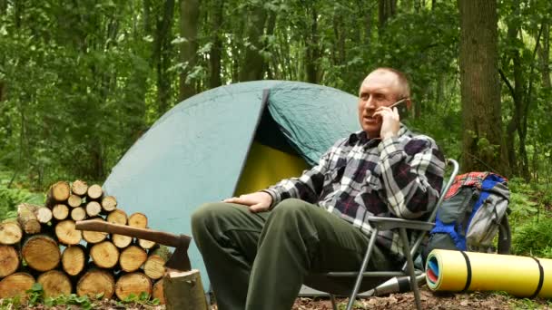 微笑成人游客在帐篷附近休息在木谈话由移动智能手机 — 图库视频影像