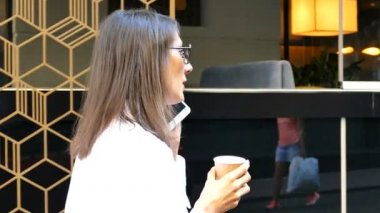 Ağır çekim. Ciddi çekici iş kadını, şehir Sokağı'nda yürüyüş... Kahve ve smartphone. 