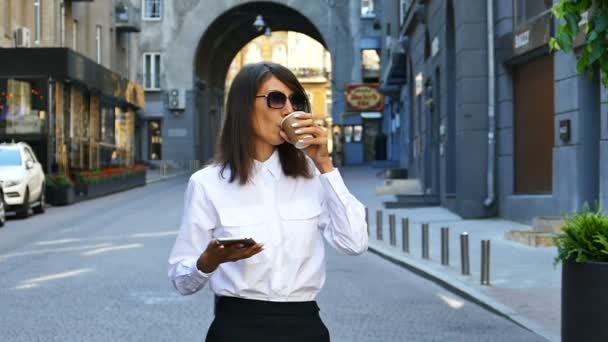 Zpomalený pohyb. Obchodní žena chůzi na ulici, pít kávu a podívat se na Smartphone