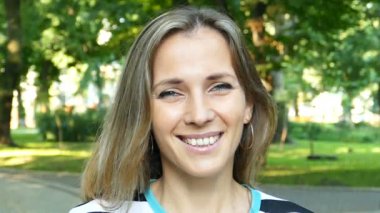 Ağır çekim. Şehirde genç güzel kadın kamera gülümsüyor parlak park. Yüzünü kapat