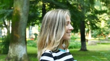 Ağır çekim. Güzel kadın şehir parkta yürümek ve kamera gülümse. Yüz yakın çekim, sürekli çekim