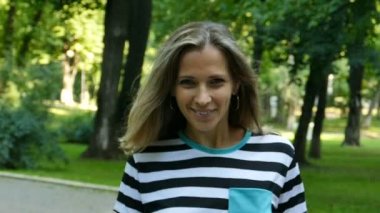 Ağır çekim. Güzel kadın şehir parkta yürümek ve kamera gülümse.