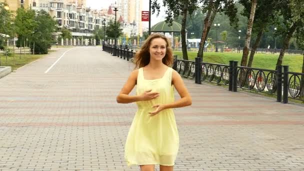 街上幸せな長い髪の少女黄色のドレスで踊る スローモーション フロント ビュー — ストック動画