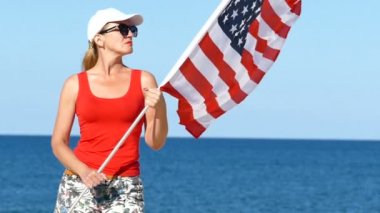 Deniz kenarında Amerikan bayrağı ile parlak yetişkin kadın stand. Ağır çekim