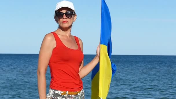 严肃的女子站在海边挂着乌克兰国旗 看着镜头 慢动作 — 图库视频影像