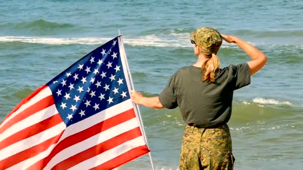 Soldat Kvinna Salute Med Amerikanska Flaggan Nära Seacoast Slow Motion — Stockvideo