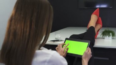4. iş kadını ile tablet, yeşil perde. Masada kırmızı moda ayakkabılar bacaklar