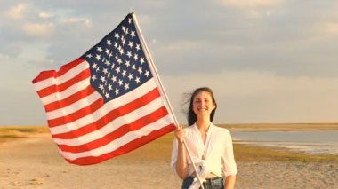 Uzun saçlı kız vatansever genç stand Amerikan bayrağı ve gülümseme ile. Ağır çekim