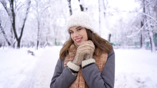 冬天城市公园里戴着白帽子的年轻女子戴上手套 微笑着在镜头里微笑 — 图库视频影像