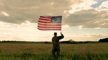 Asker sahada stand ve gökyüzü karşı Amerikan bayrağı tutun. Yavaş hareket