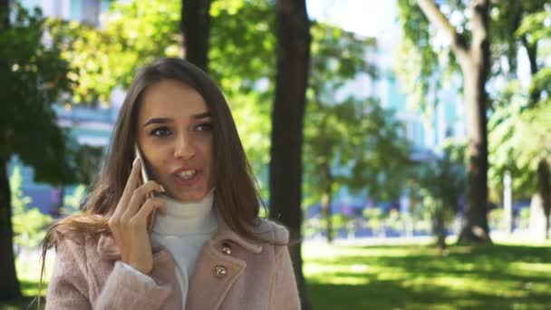 若いロングヘア女性話日当たりの良い都市公園における携帯電話スマート フォン — ストック動画