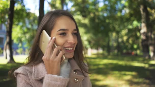 日当たりの良い都市公園におけるスマート フォンで若いきれいな女性を笑顔の話 — ストック動画