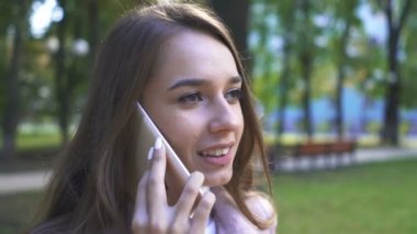   4k. güneşli şehir parkında Smartphone tarafından genç gülümseyen kadın konuşma. Sabit atış