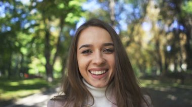   4k. güneşli şehir parkında genç güzel çekici kadının yüz kamera gülümsüyor. Portre