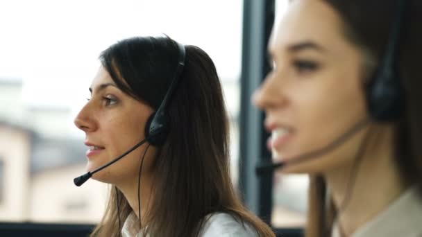 4K. Call center. Two young pretty women operators talk with client by earphones