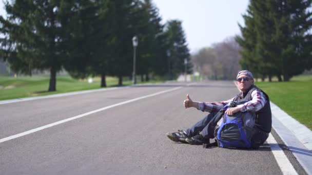 积极的成年男子搭便车在空旷的道路上 滑块拍摄 — 图库视频影像