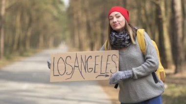 Otostop çeken kız, Los Angeles posteri ile boş yolda ahşap ta kalıyor. Bekleyen araba 