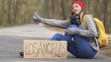 Arabayı bekliyorum. Otostop kız poster Los Angeles ile ahşap boş yolda oturup. 