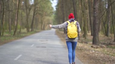 Seyahat Otostop kız ahşap boş yolda gitmek . Parmak yukarı, geri görünüm, sabit çekim