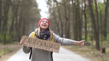 Genç otostopçu kadın California posteriyle yola çıkıyor. Arka plan