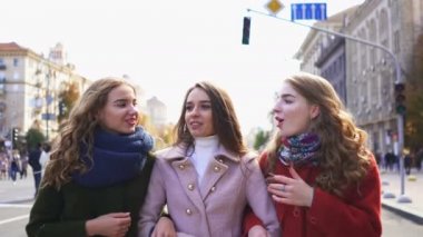   4k. Üç genç çekici kadın kız gülerek şehir caddesinde yürümek. Sabit atış