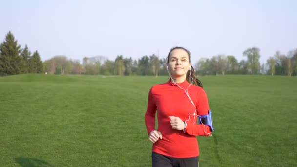 Szczęśliwa Kobieta Biegacz Biegać Zielonym Polu Czerwone Ubrania Słuchaj Muzyki — Wideo stockowe