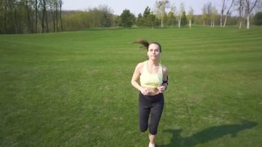 4 k. Yetişkin sportif kadın koşucu yeşil alanda çalıştırın. Kulaklıkla müzik dinleyin