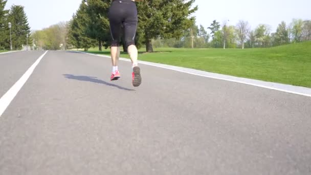 4Kスポーティーな女子ランナーの足が道路を走る イヤホンで音楽を聴く — ストック動画