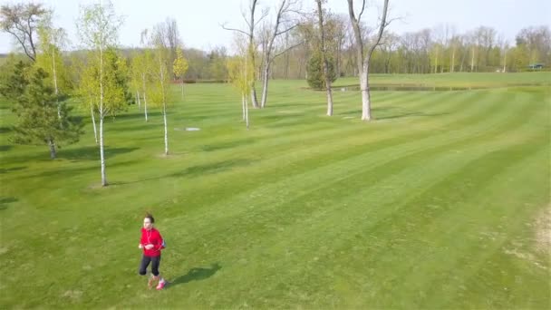 女子健身跑跑在春天的绿色场地上 摄像机倾角向下 — 图库视频影像
