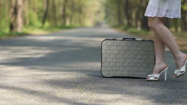 道路上のレトロなスーツケースの近くにハイヒールの靴の女性の4K — ストック動画
