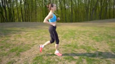 4 k. Kadın koşucu yeşil alanda koşuyor, kulaklıkla müzik dinliyor. Sabit atış, sağlıklı yaşam