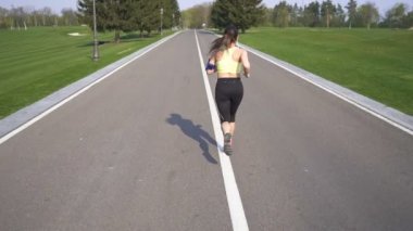 Kadın koşucu boş yolda koşuyor. Kulaklıklar. Yavaş çekim, arka plan