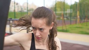 Yavaş çekim. Genç kadın boksör eğitim sokak şehir eğitim alanında çanta kumlama ile. Sabit atış, yakın yüz