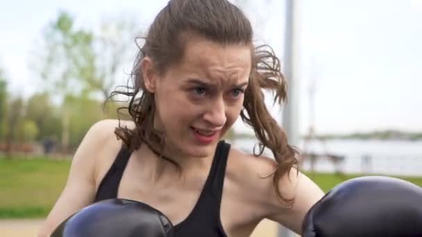 スローモーション ストリートシティのトレーニンググラウンドでパンチバッグを持つ深刻な女性ボクサーのトレーニング 安定したショット 顔をクローズアップ 自衛隊 — ストック動画