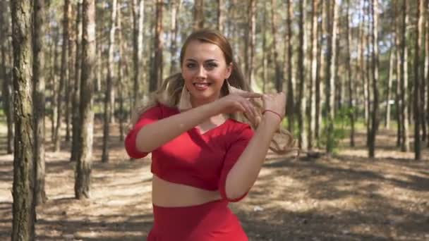 当代技巧女舞者身着红色礼服在森林中跳舞 看相机 — 图库视频影像
