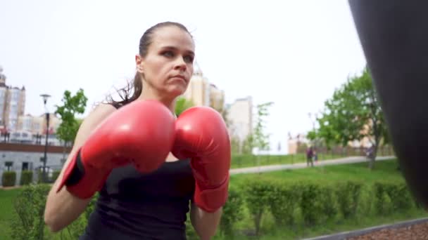 ボクシングバッグで深刻な大人の女性ボクサーのトレーニング 市立公園屋外 安定したショット スローモーション — ストック動画